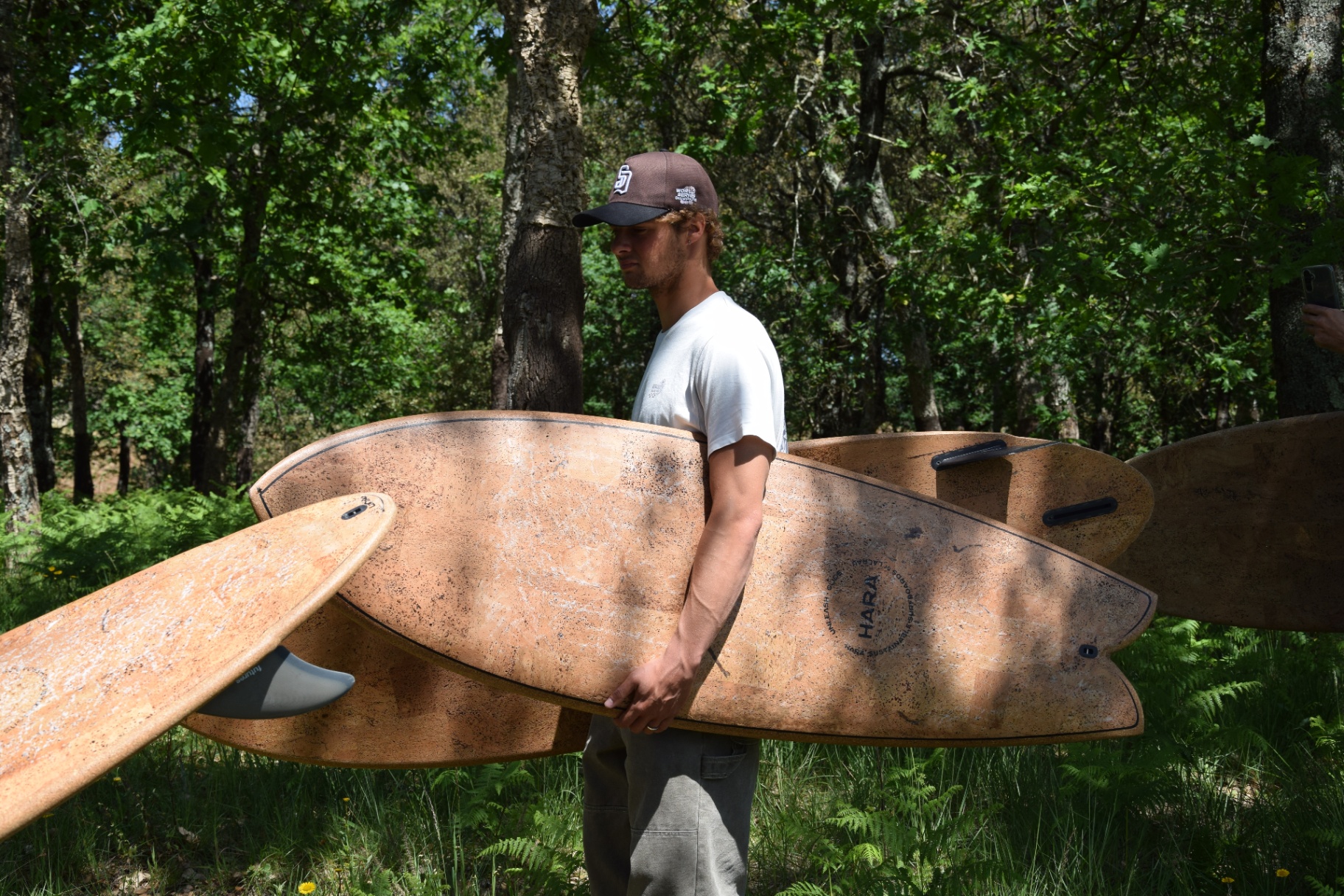 Shaper with a Hara cork surfboard in front of stacked cork bark